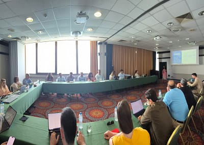 Group of people attending an indoor stakeholder meeting or workshop, seated in rows, with a presentation in progress.
